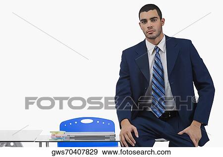 Stock Photo - Portrait of a businessman sitting on a desk in an office. Fotosearch