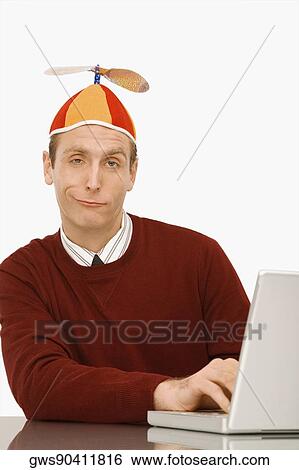 Portrait of a businessman wearing a propeller beanie and working on a laptop View Large Photo Image Stock Photograph - Portrait of a businessman wearing a propeller beanie and working on a laptop. Fotosearch
