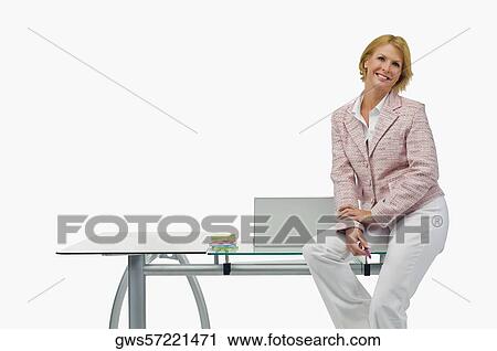 Stock Image - Portrait of a businesswoman sitting on a table and smiling. Fotosearch