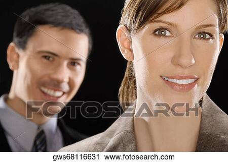 Portrait of a businesswoman smiling with a businessman behind her View Large Photo Image Stock Image - Portrait of a businesswoman smiling with a businessman behind her. Fotosearch