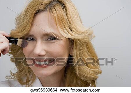 Portrait of a mature woman applying blush on her cheek and smiling View Large Photo Image Picture - Portrait of a mature woman applying blush on her cheek and smiling. Fotosearch