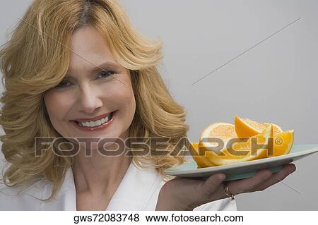 Portrait of a mature woman holding a plate of oranges and smiling View Large Photo Image Stock Photo - Portrait of a mature woman holding a plate of oranges and smiling. Fotosearch