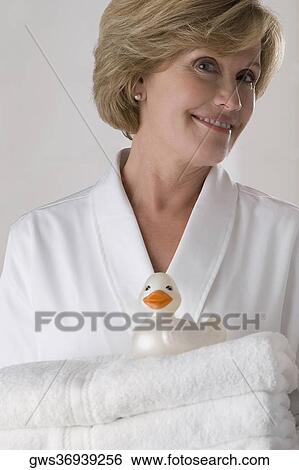 Stock Photograph - Portrait of a mature woman holding a stack of folded towels and smiling. Fotosearch