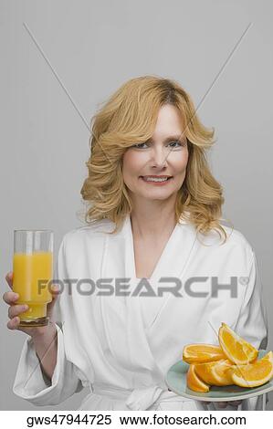 Stock Photography - Portrait of a mature woman holding a plate of oranges and a glass of orange juice. Fotosearch