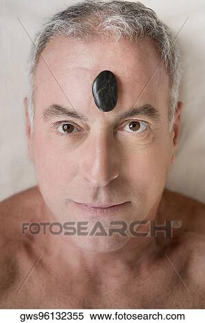 Stock Photography - Portrait of a senior man lying on a massage table with a pebble on his forehead. Fotosearch