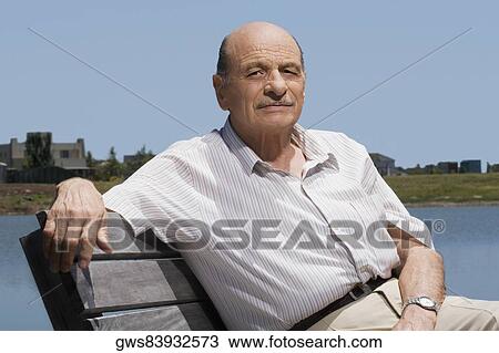 Stock Image - Portrait of a senior man sitting on a bench at the lakeside. Fotosearch
