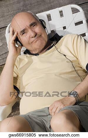 Stock Photography - Portrait of a senior man sitting on a chair and listening to music. Fotosearch