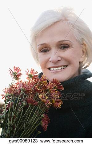 Stock Image - Portrait of a senior woman holding bunch of flowers and smiling. Fotosearch