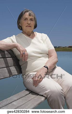 Portrait of a senior woman sitting on a bench at the lakeside View Large Photo Image Picture - Portrait of a senior woman sitting on a bench at the lakeside. Fotosearch