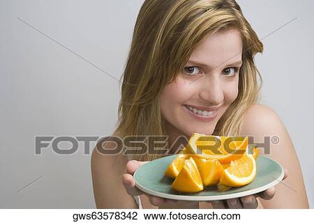 Stock Image - Portrait of a teenage girl holding a plate of oranges and smiling. Fotosearch