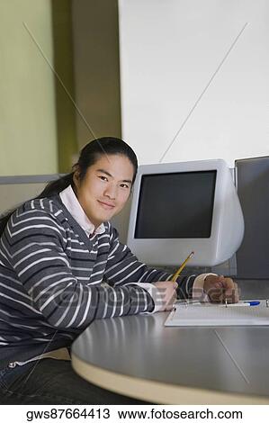 Stock Image - Portrait of a young man sitting in a classroom and writing. Fotosearch
