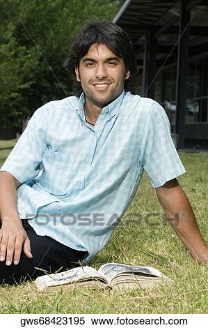 Portrait of a young man sitting in a lawn and smiling View Large Photo Image Stock Photography - Portrait of a young man sitting in a lawn and smiling. Fotosearch