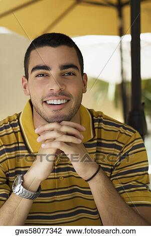 Stock Image - Portrait of a young man smiling with his hands clasped. Fotosearch