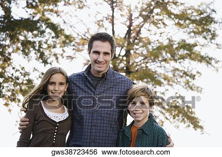 Portrait of a young man standing with his two children and smiling View Large Photo Image Stock Photograph - Portrait of a young man standing with his two children and smiling. Fotosearch