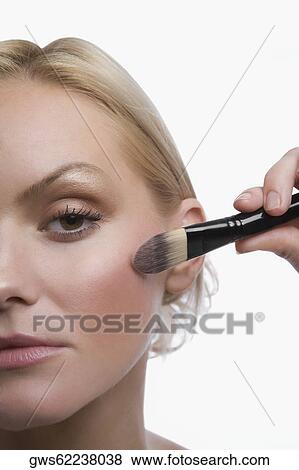 Stock Photo - Portrait of a young woman applying blush on her cheek. Fotosearch