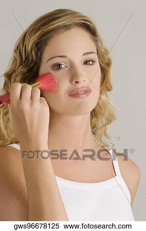 Stock Photography - Portrait of a young woman applying blush on her cheek. Fotosearch