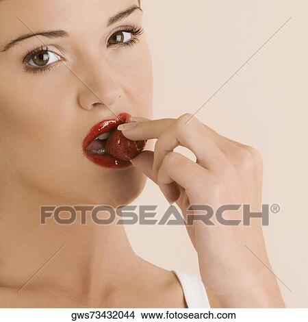 Picture - Portrait of a young woman eating a strawberry. Fotosearch