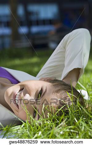 Stock Photo - Portrait of a young woman lying on grass and smiling. Fotosearch