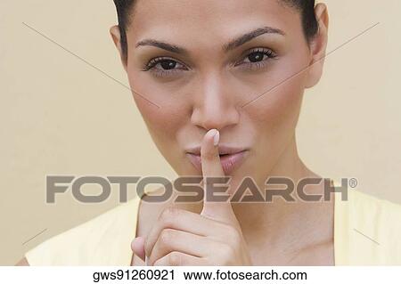 Stock Image - Portrait of a young woman putting her finger on her lips. Fotosearch