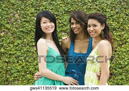 Stock Photo - Portrait of three young women smiling with arms around each other. Fotosearch