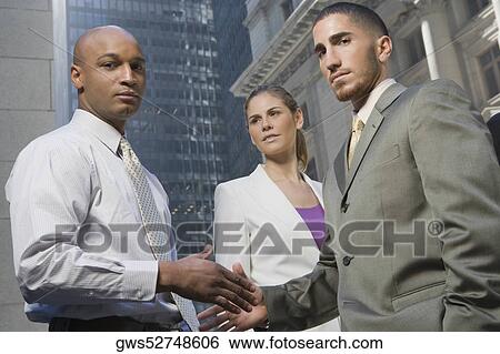 Portrait of two businessmen shaking hands with a businesswoman standing beside them View Large Photo Image Stock Photograph - Portrait of two businessmen shaking hands with a businesswoman standing beside them. Fotosearch