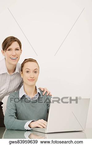 Stock Photo - Portrait of two businesswomen working on a laptop and smiling. Fotosearch