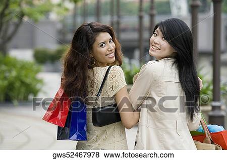 Stock Photo - Portrait of two young women carrying shopping bags and smiling. Fotosearch