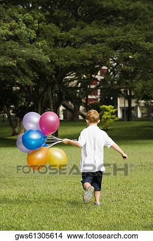 Picture - Rear view of a boy holding balloons in a park. Fotosearch