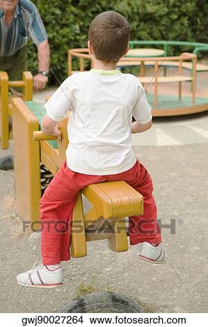 Rear view of a boy sitting on a seesaw in a park, Cinque Terre, Manarola, La Spezia, Liguria, Italy View Large Photo Image Picture - Rear view of a boy sitting on a seesaw in a park, Cinque Terre, Manarola, La Spezia, Liguria, Italy. Fotosearch
