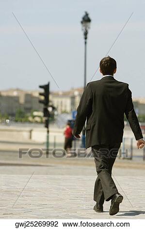 Stock Image - Rear view of a businessman walking on a sidewalk, Bordeaux, Aquitaine, France. Fotosearch