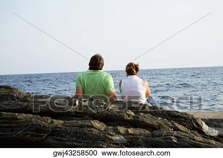 Rear view of a couple sitting at the seaside, Italian Riviera, Mar Ligure, Genoa, Liguria, Italy View Large Photo Image Stock Image - Rear view of a couple sitting at the seaside, Italian Riviera, Mar Ligure, Genoa, Liguria, Italy. Fotosearch