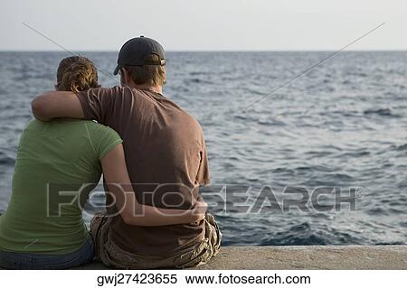 Stock Photography - Rear view of a couple sitting at the seaside, Italian Riviera, Mar Ligure, Genoa, Liguria, Italy. Fotosearch