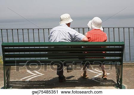 Rear view of a couple sitting on a bench at seaside, Via Aniello Califano, Bay of Naples, Sorrento, Sorrentine Peninsula, Naples Province, Campania, Italy View Large Photo Image Stock Image - Rear view of a couple sitting on a bench at seaside, Via Aniello Califano, Bay of Naples, Sorrento, Sorrentine Peninsula, Naples Province, Campania, Italy. Fotosearch