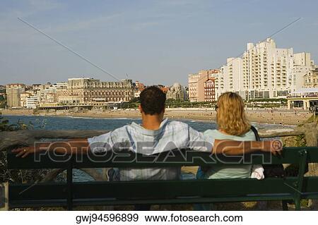 Rear view of a couple sitting on a bench, Grande Plage, Hotel du Palais, Biarritz, France View Large Photo Image Stock Photo - Rear view of a couple sitting on a bench, Grande Plage, Hotel du Palais, Biarritz, France. Fotosearch