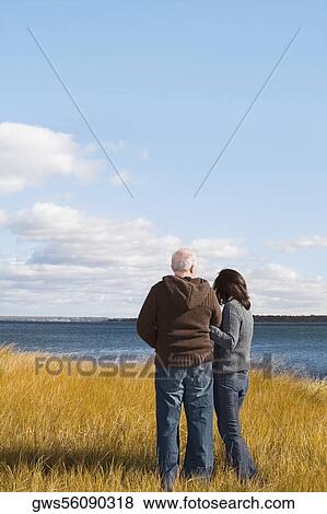 Stock Photo - Rear view of a couple standing on the beach with arm in arm. Fotosearch