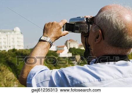 Stock Image - Rear view of a man filming with his home video camera, Biarritz, Basque Country, Pyrenees-Atlantiques, Aquitaine, France. Fotosearch