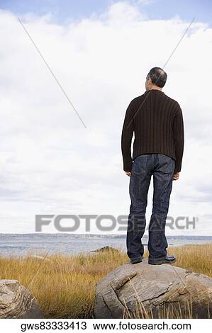 Stock Image - Rear view of a mature man standing on a rock. Fotosearch