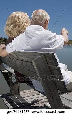 Rear view of a senior couple sitting on a bench at the lakeside View Large Photo Image Stock Photo - Rear view of a senior couple sitting on a bench at the lakeside. Fotosearch