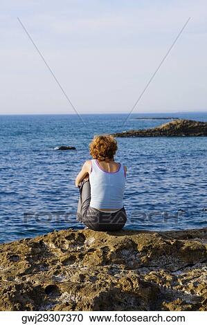Rear view of a woman sitting on a rock, Baie de Biarritz, Biarritz, Pyrenees-Atlantiques, France View Large Photo Image Stock Image - Rear view of a woman sitting on a rock, Baie de Biarritz, Biarritz, Pyrenees-Atlantiques, France. Fotosearch