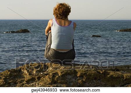Rear view of a woman sitting on a rock, Baie De Biarritz, Biarritz, Pyrenees-Atlantiques, France View Large Photo Image Stock Image - Rear view of a woman sitting on a rock, Baie De Biarritz, Biarritz, Pyrenees-Atlantiques, France. Fotosearch