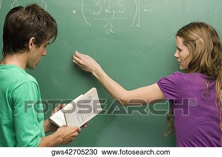 Rear view of a young woman writing on a blackboard with a young man reading a book beside her View Large Photo Image Stock Image - Rear view of a young woman writing on a blackboard with a young man reading a book beside her. Fotosearch