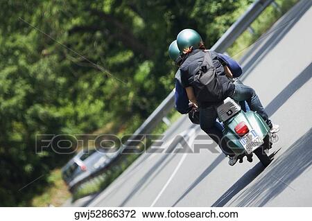 Stock Image - Rear view of two persons on a motor scooter, Via Aurelia, Italian Riviera, Liguria, Italy. Fotosearch