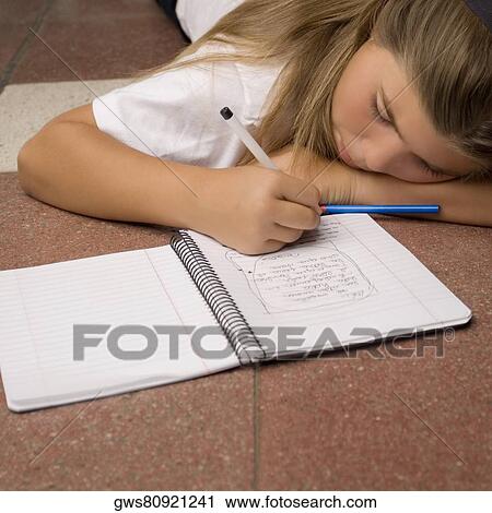 Stock Image - Schoolgirl lying on the floor and writing in a spiral notebook. Fotosearch