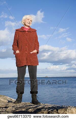 Senior woman standing on a rock at the coast View Large Photo Image Stock Image - Senior woman standing on a rock at the coast. Fotosearch
