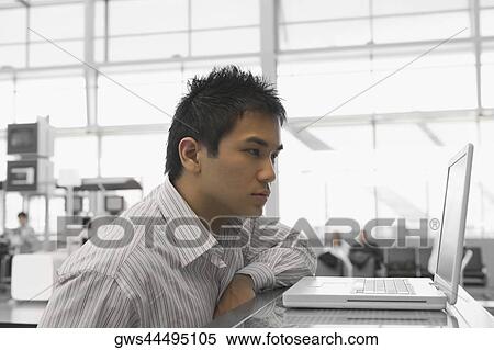 Side profile of a businessman looking at a laptop at an airport check-in counter View Large Photo Image Stock Photography - Side profile of a businessman looking at a laptop at an airport check-in counter. Fotosearch