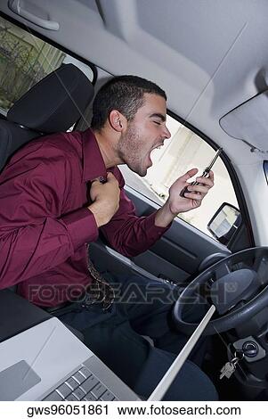 Stock Image - Side profile of a businessman sitting in a car and shouting. Fotosearch