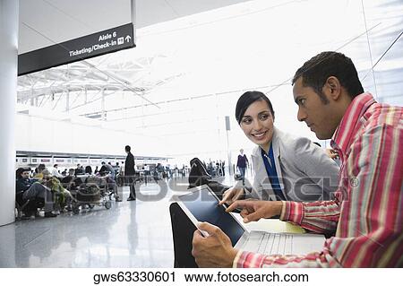 Stock Image - Side profile of a businessman using a laptop with a businesswoman sitting beside him at an airport. Fotosearch