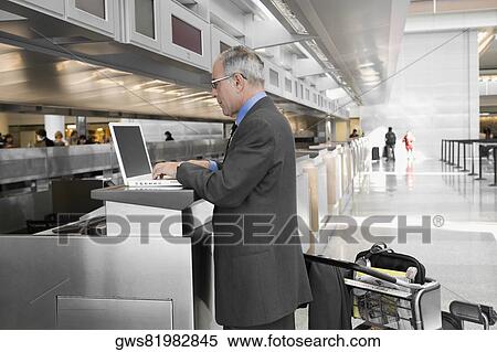 Side profile of a businessman using a laptop at an airport check-in counter View Large Photo Image Stock Photography - Side profile of a businessman using a laptop at an airport check-in counter. Fotosearch