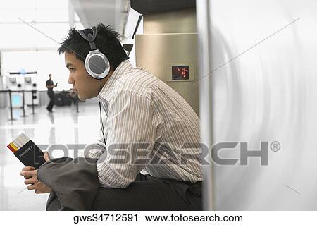 Side profile of a businessman wearing listening to headphones at an airport View Large Photo Image Stock Image - Side profile of a businessman wearing listening to headphones at an airport. Fotosearch