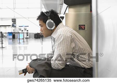Side profile of a businessman wearing listening to headphones at an airport View Large Photo Image Stock Photography - Side profile of a businessman wearing listening to headphones at an airport. Fotosearch